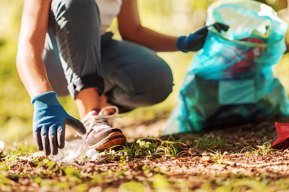 A woman picks up trash in a park and puts them in a trash bag.