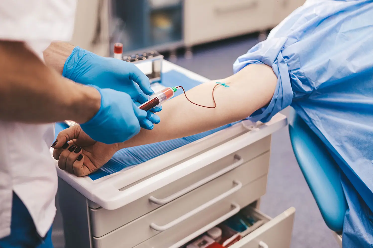 A medical technician wearing surgical gloves is taking a blood sample from a patient.