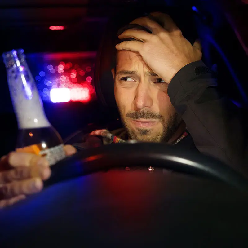A bearded man is drinking a bottle of beer while driving and is caught by police.