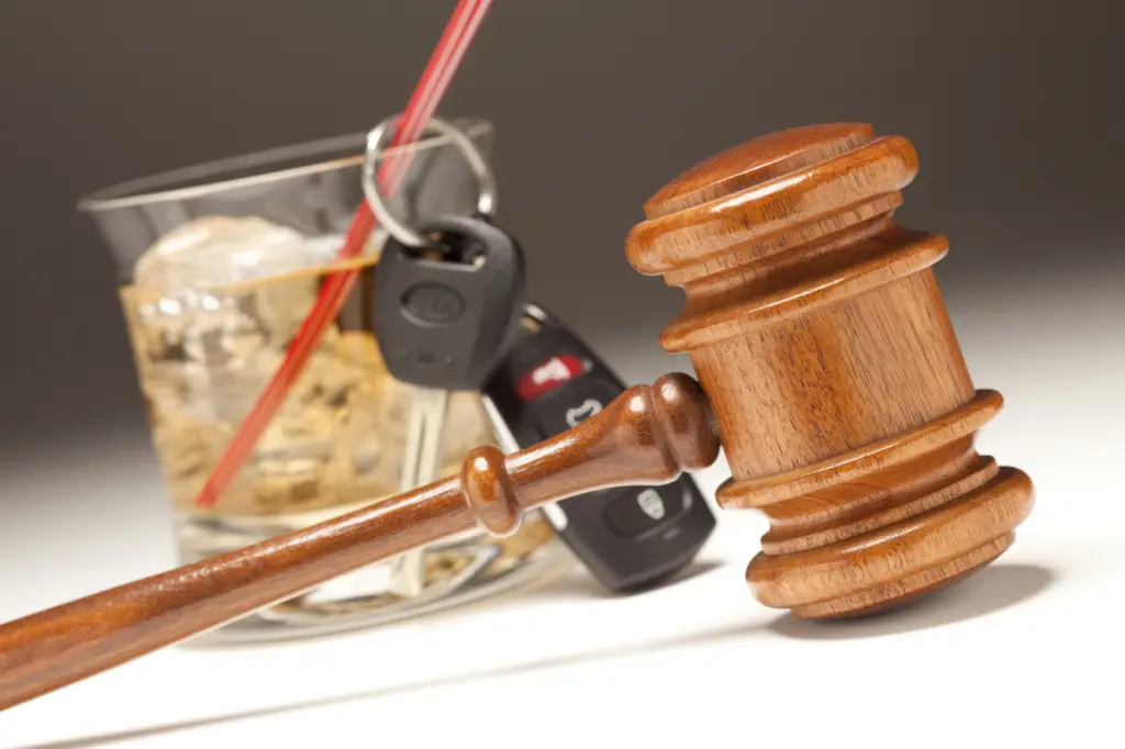 a wooden gavel is in the foreground and behind it is a car key and a glass with liquor.