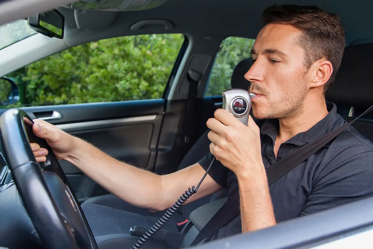 A man takes a breathalyzer test in his car.
