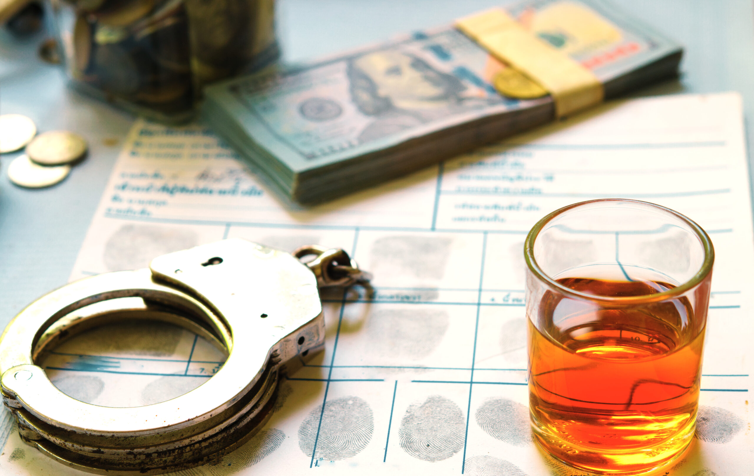 Document with fingerprints, handcuffs, alcohol, and money.